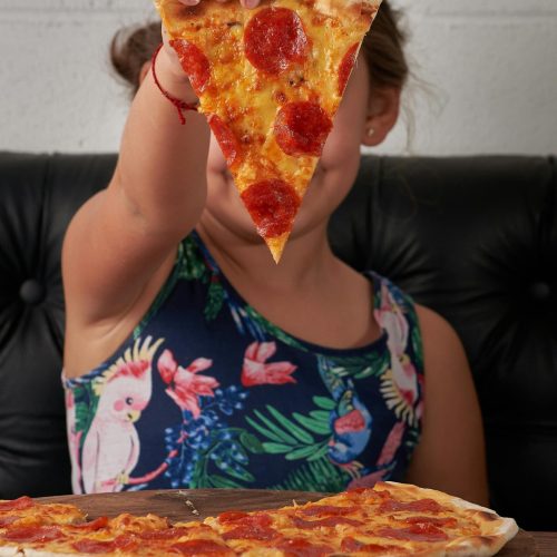 A child holding a slice of pepperoni pizza inside a restaurant.
